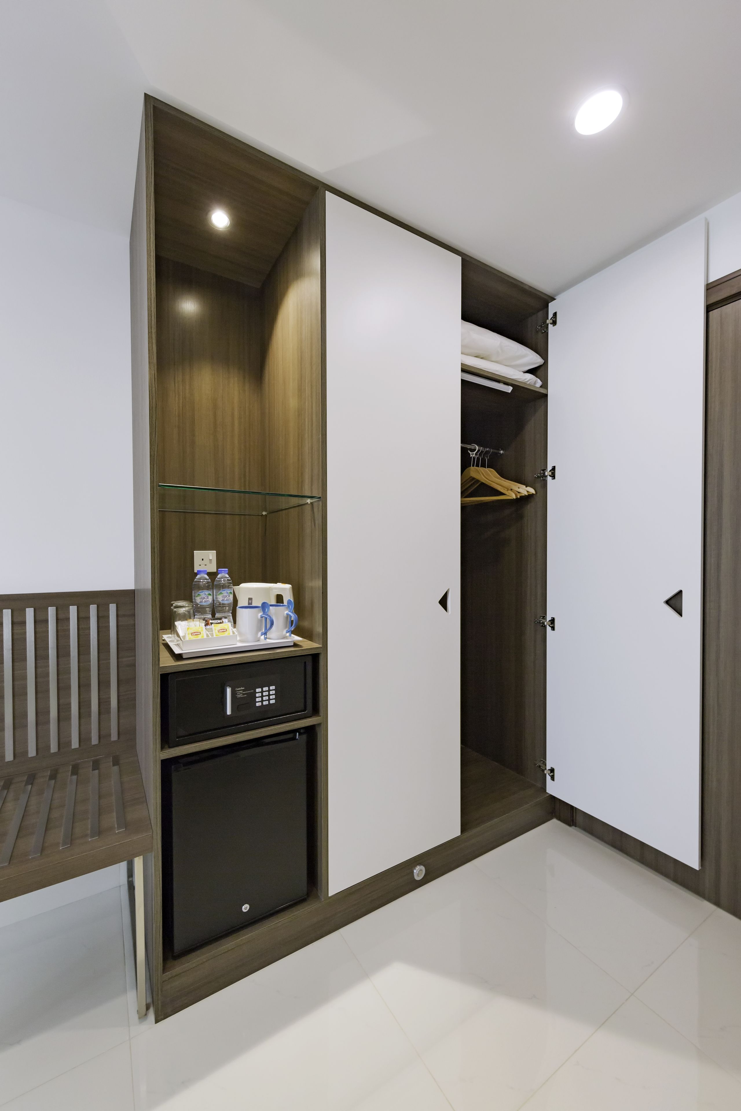 Quarto de hotel com guarda-roupa, mini-frigorífico e um banco.