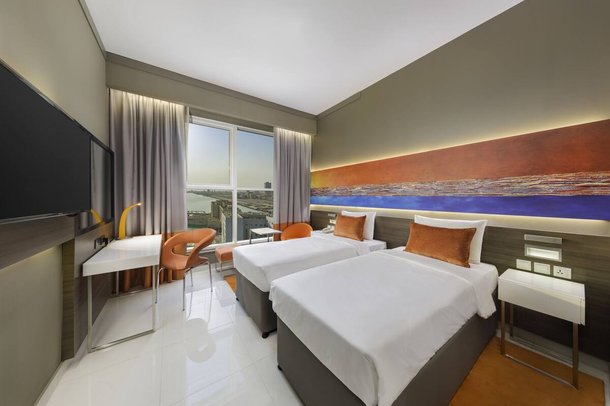 A modern hotel room with two beds, a desk, and a chair.