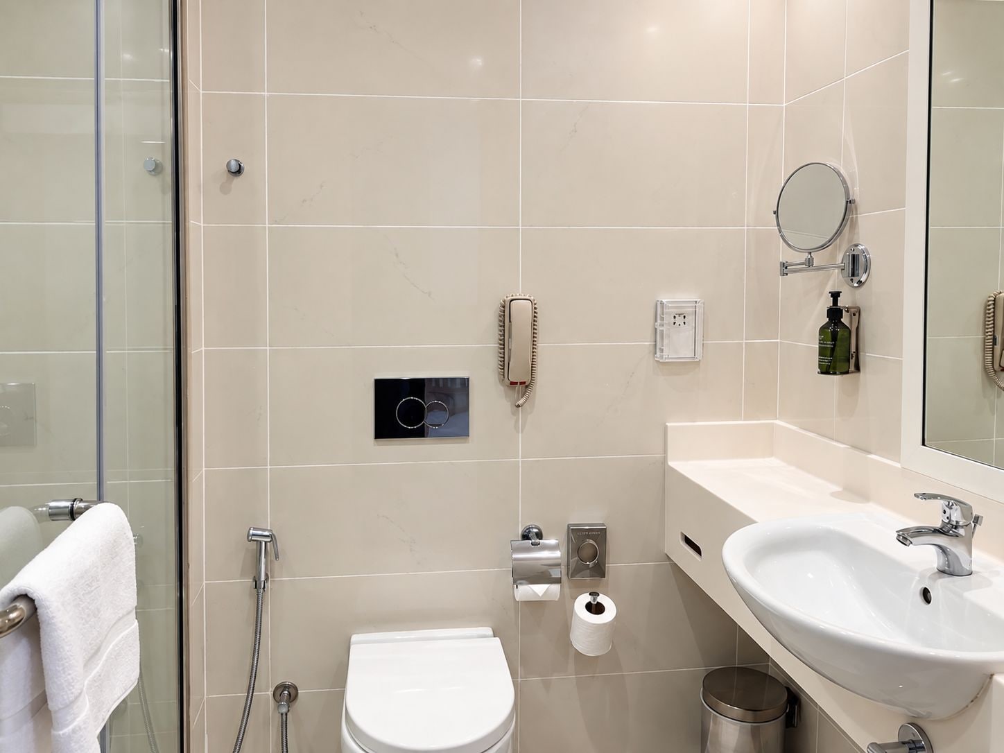 Et moderne badeværelse med en glasbrusekabine, et hvidt toilet, en vask med et spejl og en telefon.