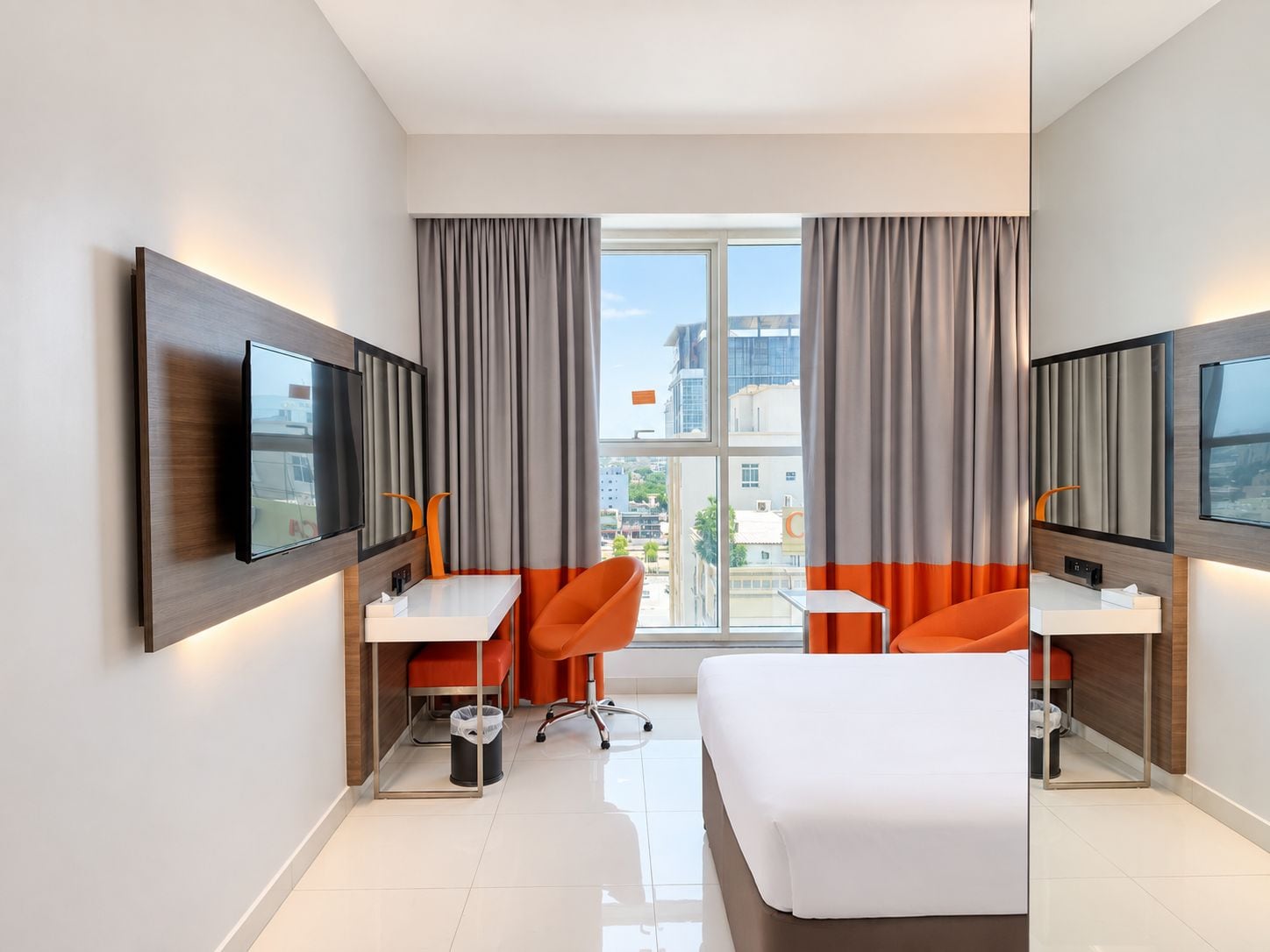 Habitación de hotel moderna con una cama grande, dos escritorios, un televisor y vista a la ciudad.