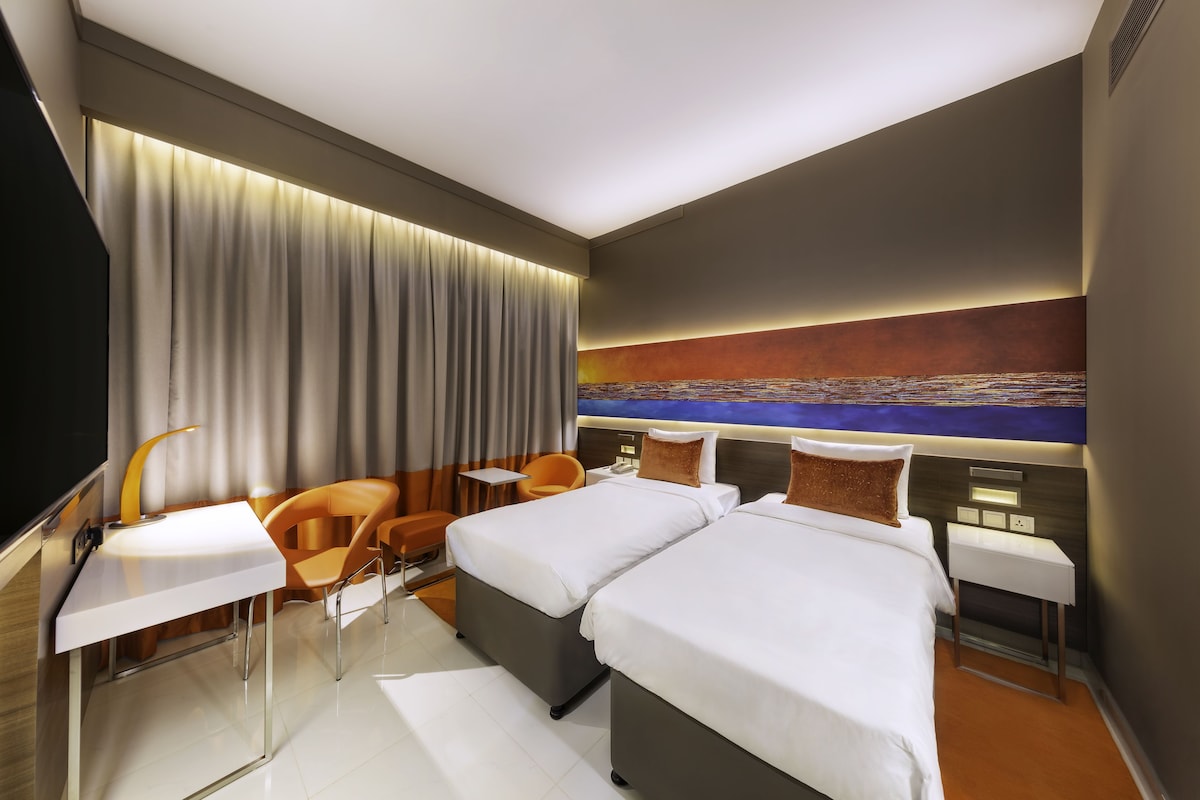 A modern hotel room with two beds, a desk, a chair, and a large abstract painting on the wall.