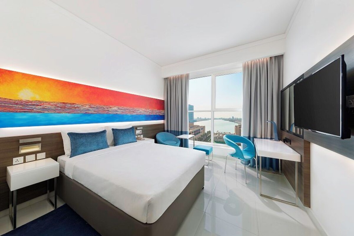 A hotel room with a large bed, a desk, a chair, and a TV.