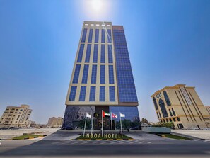 A modern hotel building with a prominent entrance, multiple flags, and a clear sky. - Nooa Hotel Ras Al Khaimah (Ras Al Khaimah)