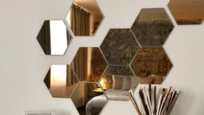 A white table with a framed certificate, a glass vase with sticks, and hexagonal mirrors reflecting a room with a bed and a lamp. - Francis B&B Superior (Trieste)