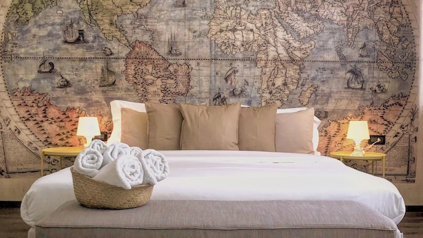 A bedroom with a large world map on the wall, a bed with white linens, and a basket of towels. - Francis B&B Superior (Trieste)