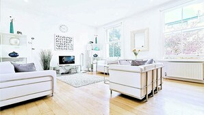 A modern living room with a flat-screen TV, white sofas, a coffee table, and large windows. - Luxury Designer Apartments Hammersmith 1 (London)