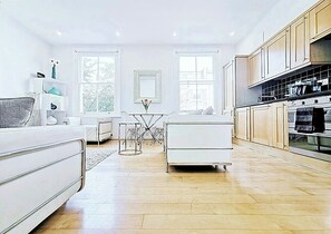 Une cuisine moderne avec des meubles en bois, un coin repas doté d’une table et de chaises blanches, et une grande fenêtre qui laisse entrer la lumière naturelle.