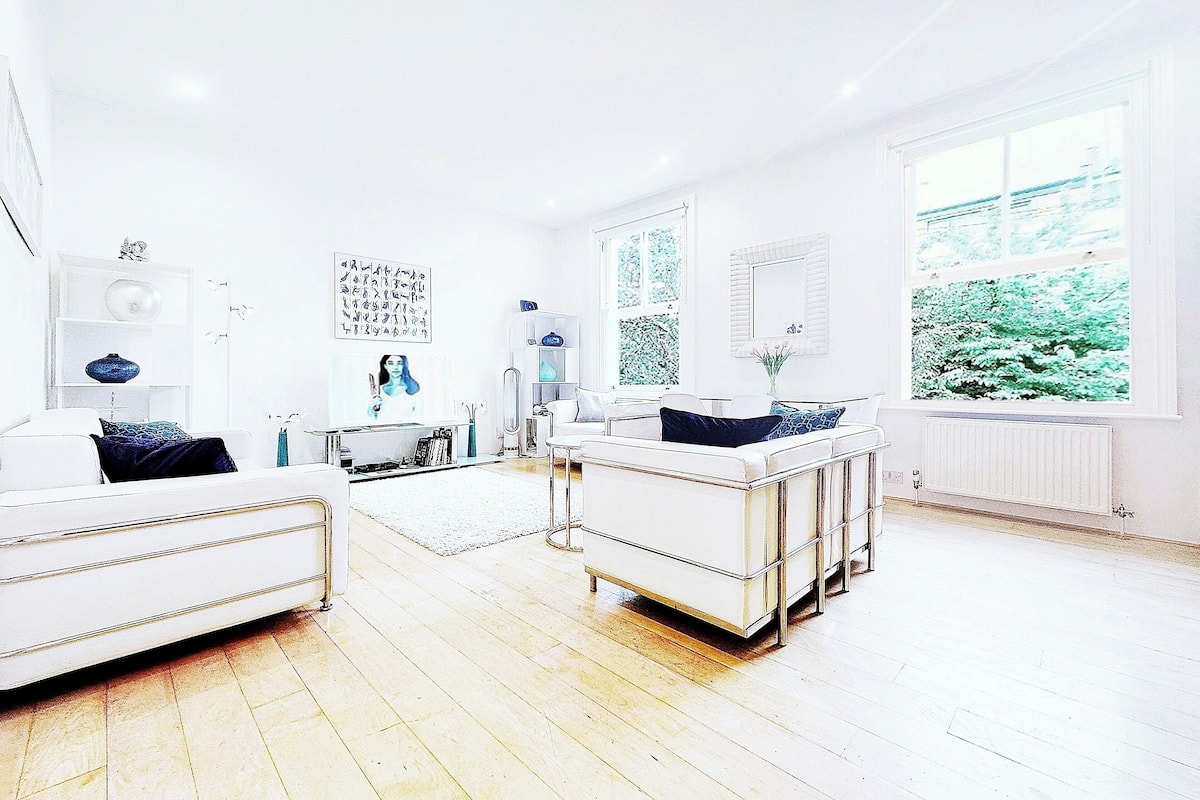 A modern living room with a white sofa, a white coffee table, and a large window with a view of greenery.
