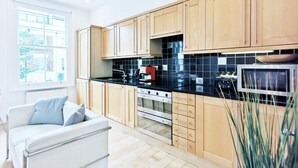 A modern kitchen with wooden cabinets, a black countertop, and a built-in oven. - Luxury Designer Apartments Hammersmith 1 (London)