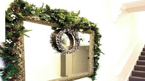 A mirror with a decorative wreath and a vase with greenery on a white console table. - Luxury Designer Apartments Hammersmith 1 (London)