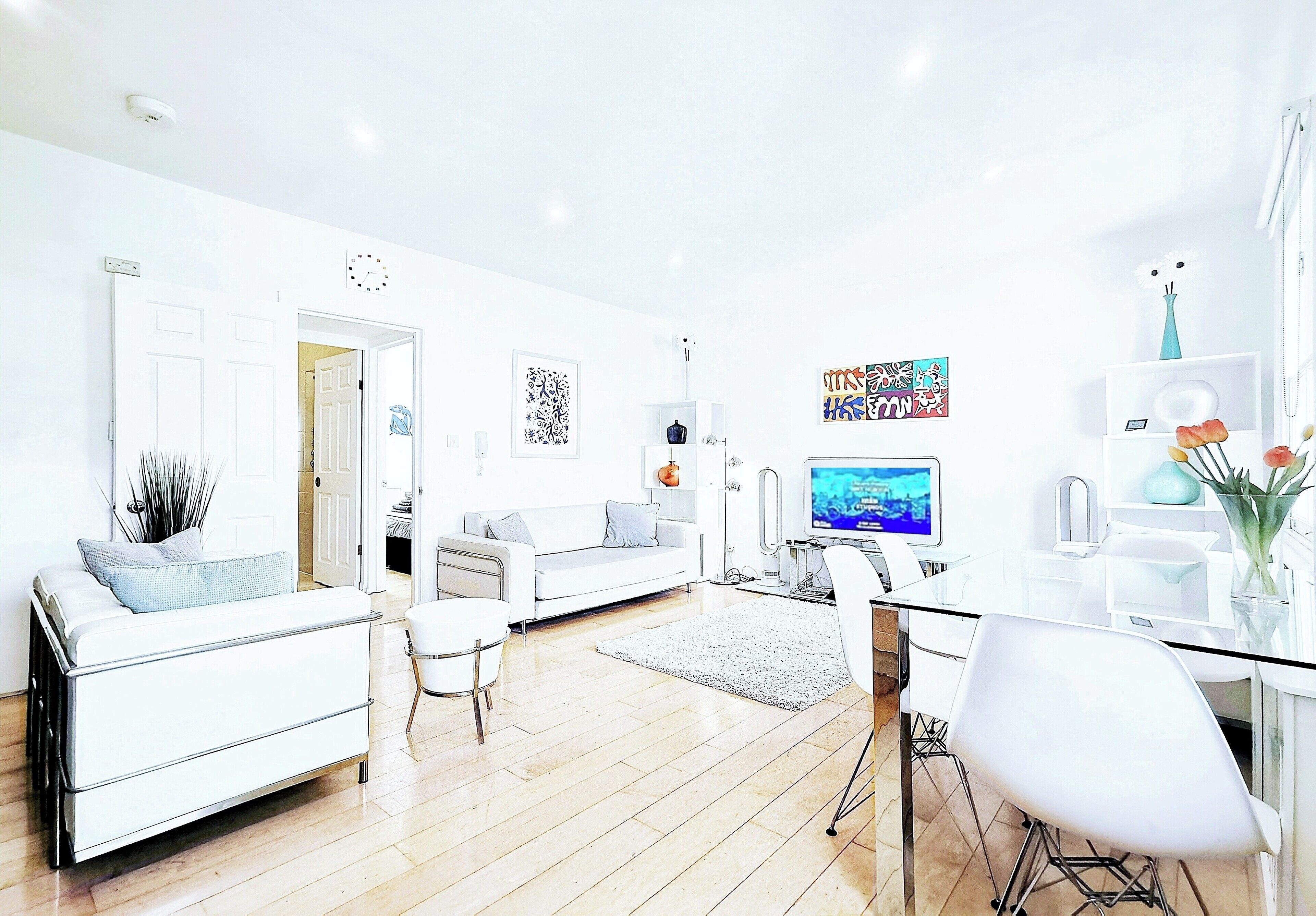 A modern living room with a white sofa, a dining table with chairs, a TV, and artwork on the walls.