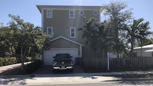 A two-story residential building with a garage, surrounded by palm trees and a wooden fence. - Private Home by Ideal Experience VR (Fort Lauderdale)