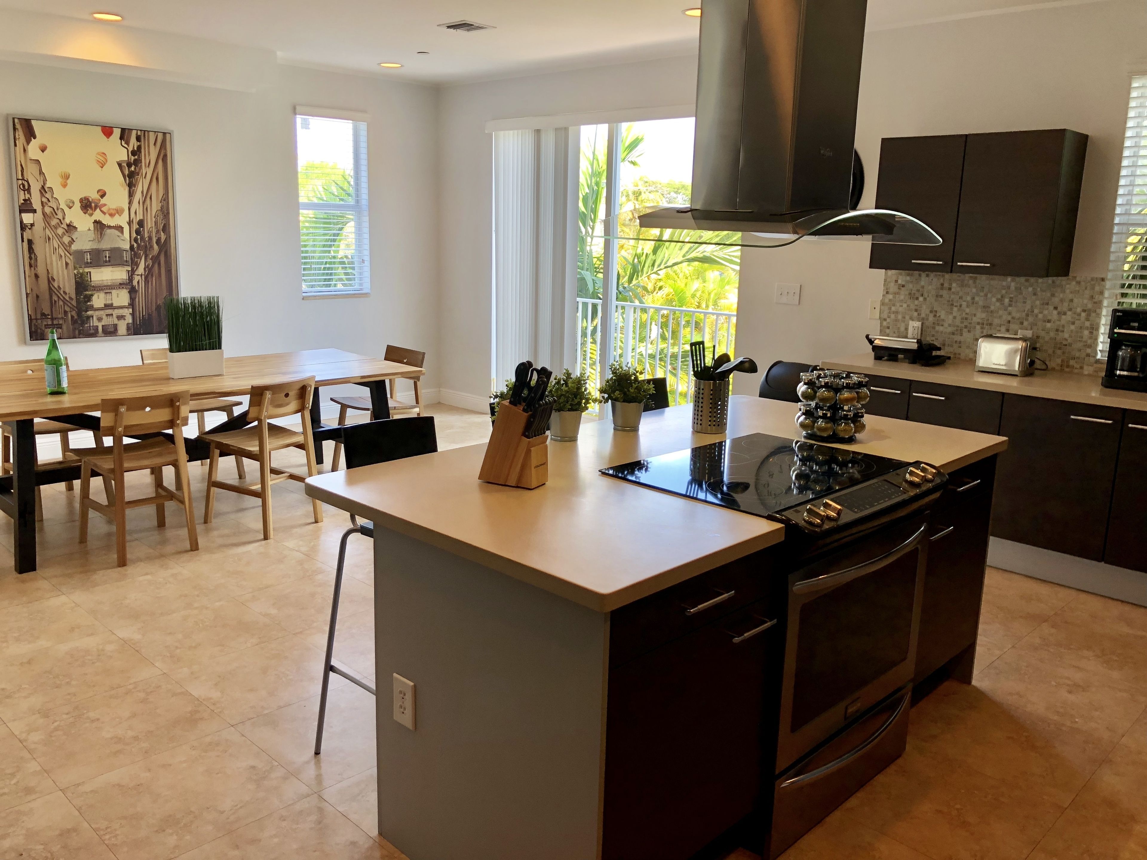 A modern kitchen with a central island, built-in oven, and a dining area with a wooden table and chairs.