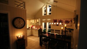 A dining area with a wooden table and chairs, a clock on the wall, and a kitchen in the background.