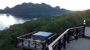 A wooden deck with a metal railing overlooking a lake and mountains.