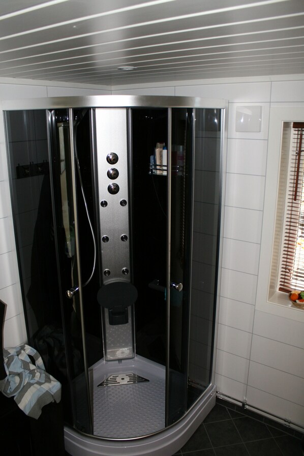 A glass-enclosed shower stall with a control panel, a towel rack, and a window with blinds. - House with stunning views !! (Sortland)