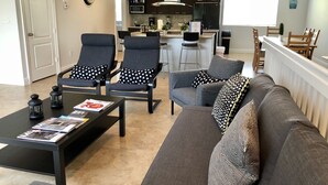 Una sala de estar moderna con un sofá gris, dos sillones negros con cojines blancos con lunares, una mesa de centro negra con revistas y una mesita auxiliar negra.