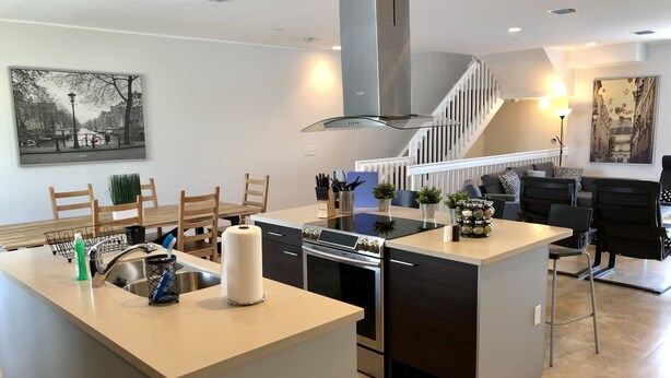 Una cocina moderna con una isla central, electrodomésticos de acero inoxidable y una escalera que lleva a un altillo.