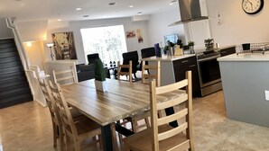 Una cocina moderna con comedor, que presenta una mesa y sillas de madera, un extractor de acero inoxidable y un reloj en la pared.