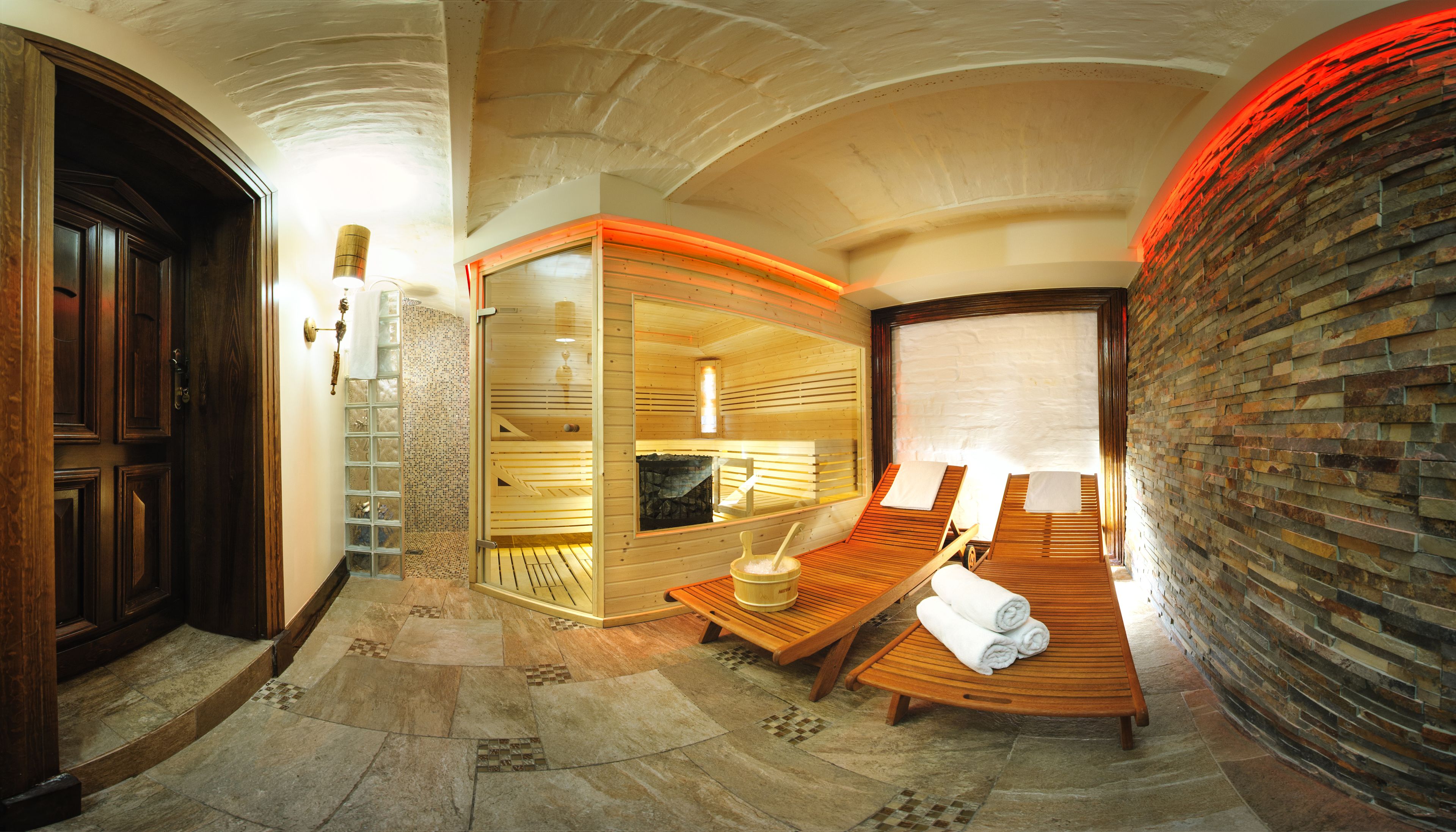A sauna room with wooden benches, a stone wall, and a wooden door.
