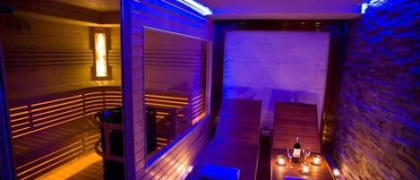 A sauna with wooden walls and benches, a table with candles, and a bottle of wine.