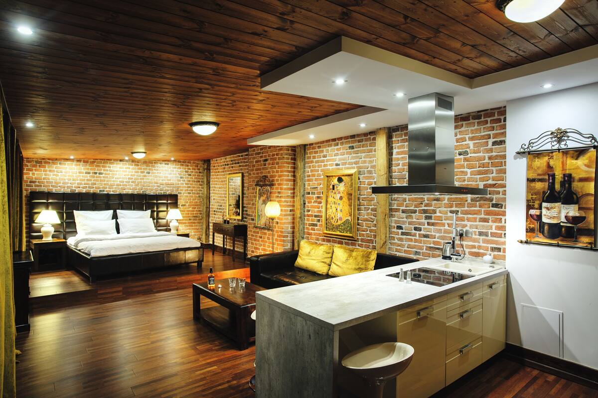 Une chambre d’hôtel comprenant un lit, un canapé, une table basse, un coin cuisine avec un évier et un mur en briques.
