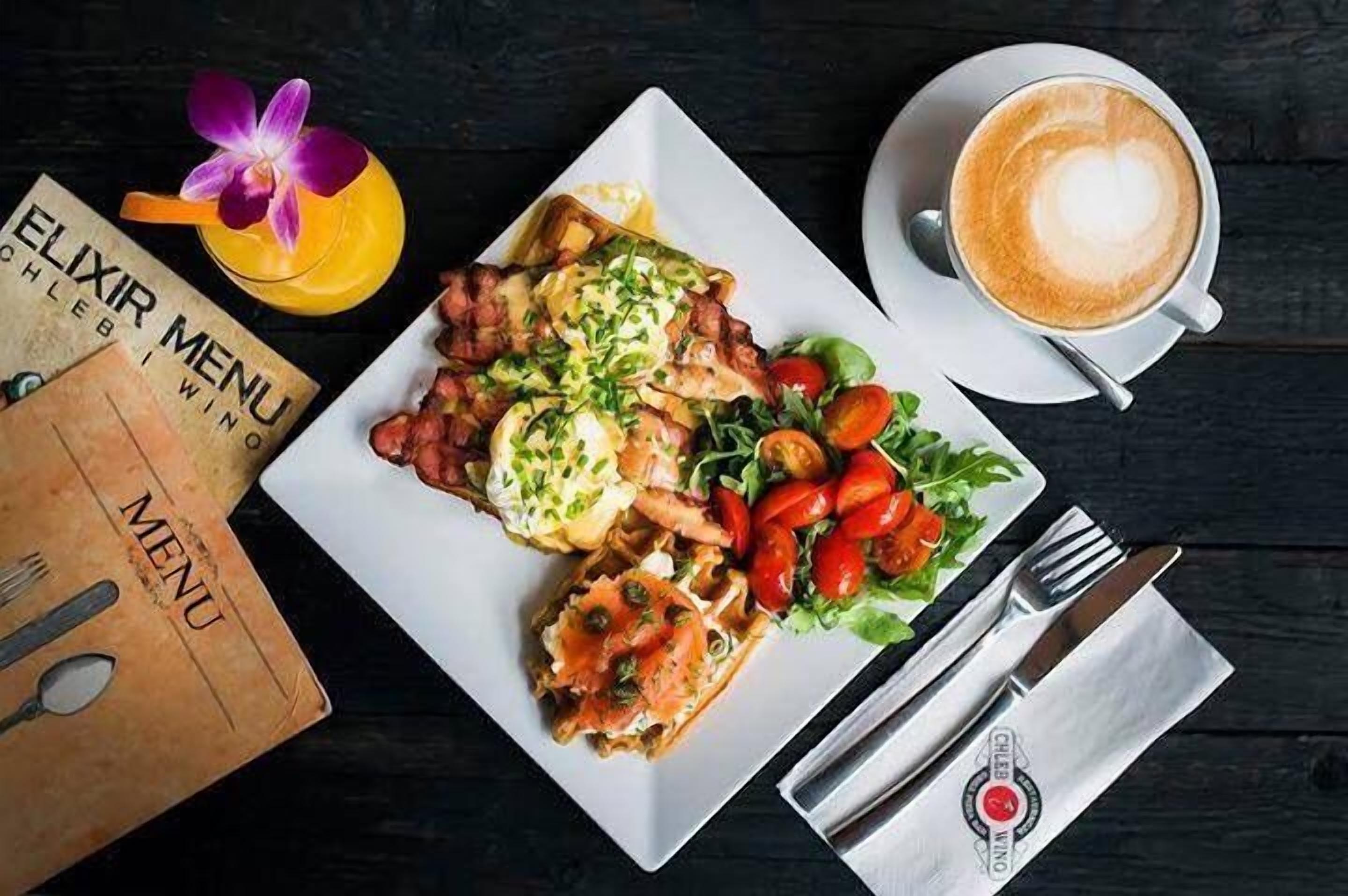 Un plato de desayuno con huevos, tocino y ensalada, una taza de café y un menú sobre una mesa de madera.
