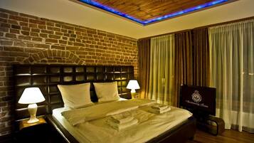 A hotel room with a brick wall, a wooden ceiling, a bed with white linens, two bedside lamps, and a television on a stand.