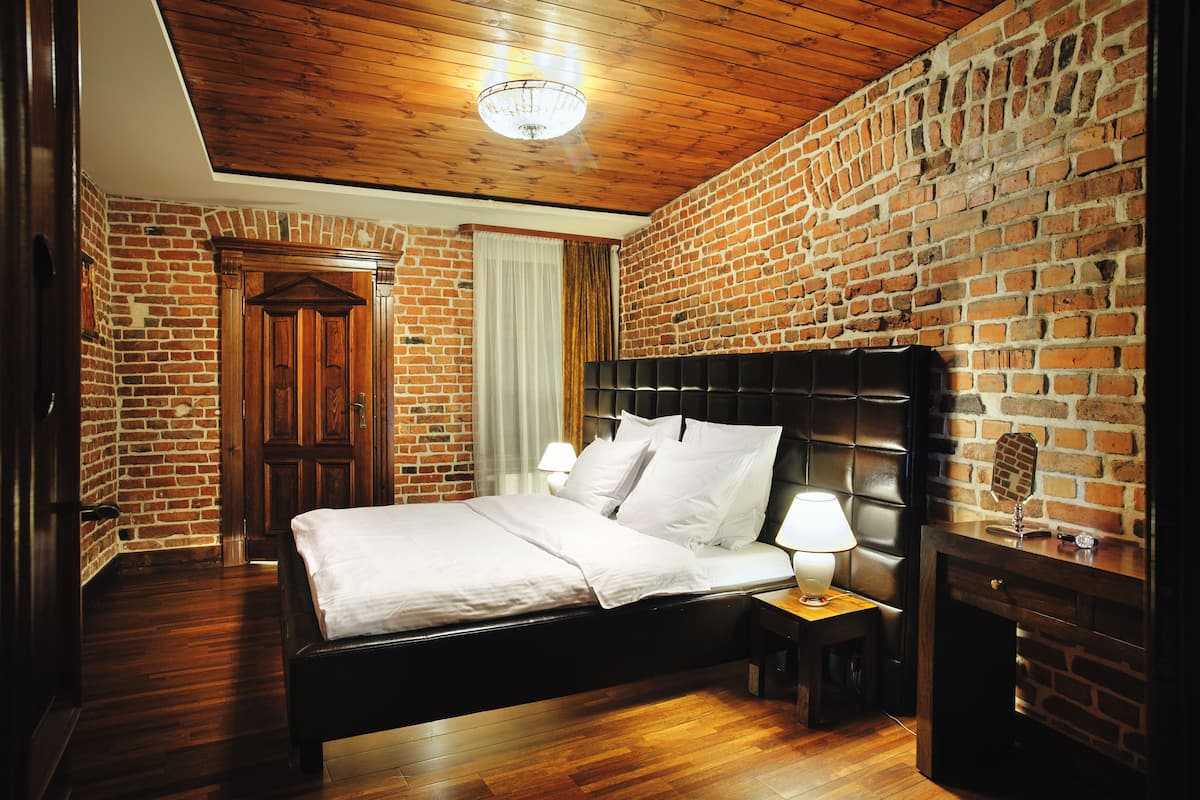 Une pièce avec un mur en briques, un plafond en bois et un lit recouvert de draps blancs.