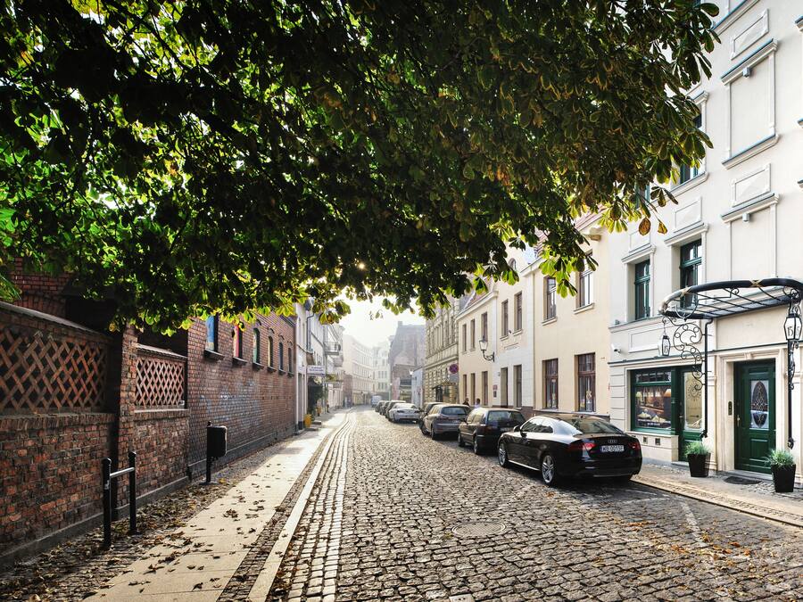 A cobblestone street lined with buildings, including a visible storefront with a sign reading "SALON FRYZERSKI".