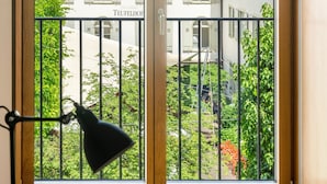 A window with a view of a building with multiple windows and balconies, a metal railing, and a small tree in the foreground. - SET Hotel.Residence by Teufelhof Basel (Basel)