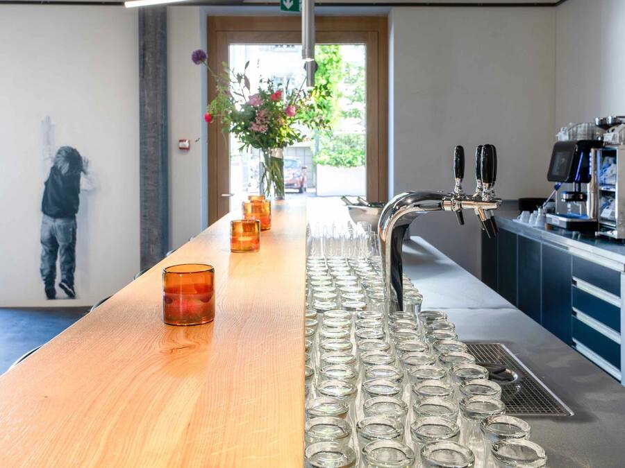Una zona de bar con una barra de madera larga, varios vasos y una cafetera.