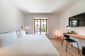 A bedroom with a bed, a desk, a chair, a lamp, and a window with a view of buildings. - SET Hotel.Residence by Teufelhof Basel (Basel)