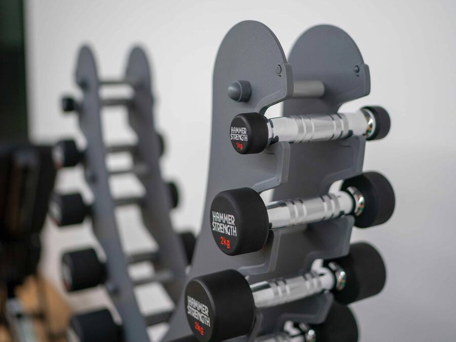 Primer plano de una torre de pesas con pesos ajustables identificados como "HAMMER STRENGTH" y "2kg".