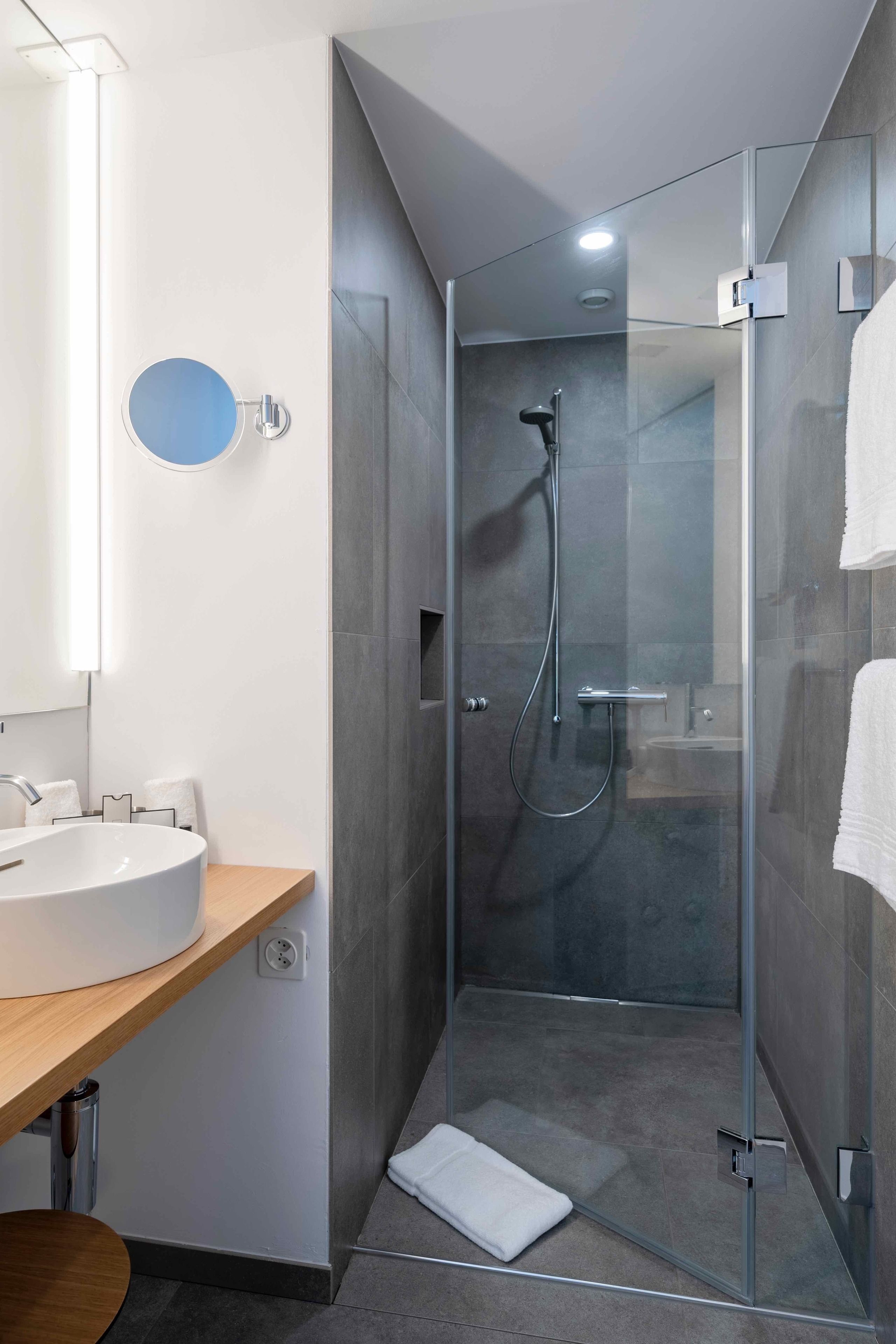 A modern bathroom with a glass-enclosed shower, a round mirror, and a wooden vanity.
