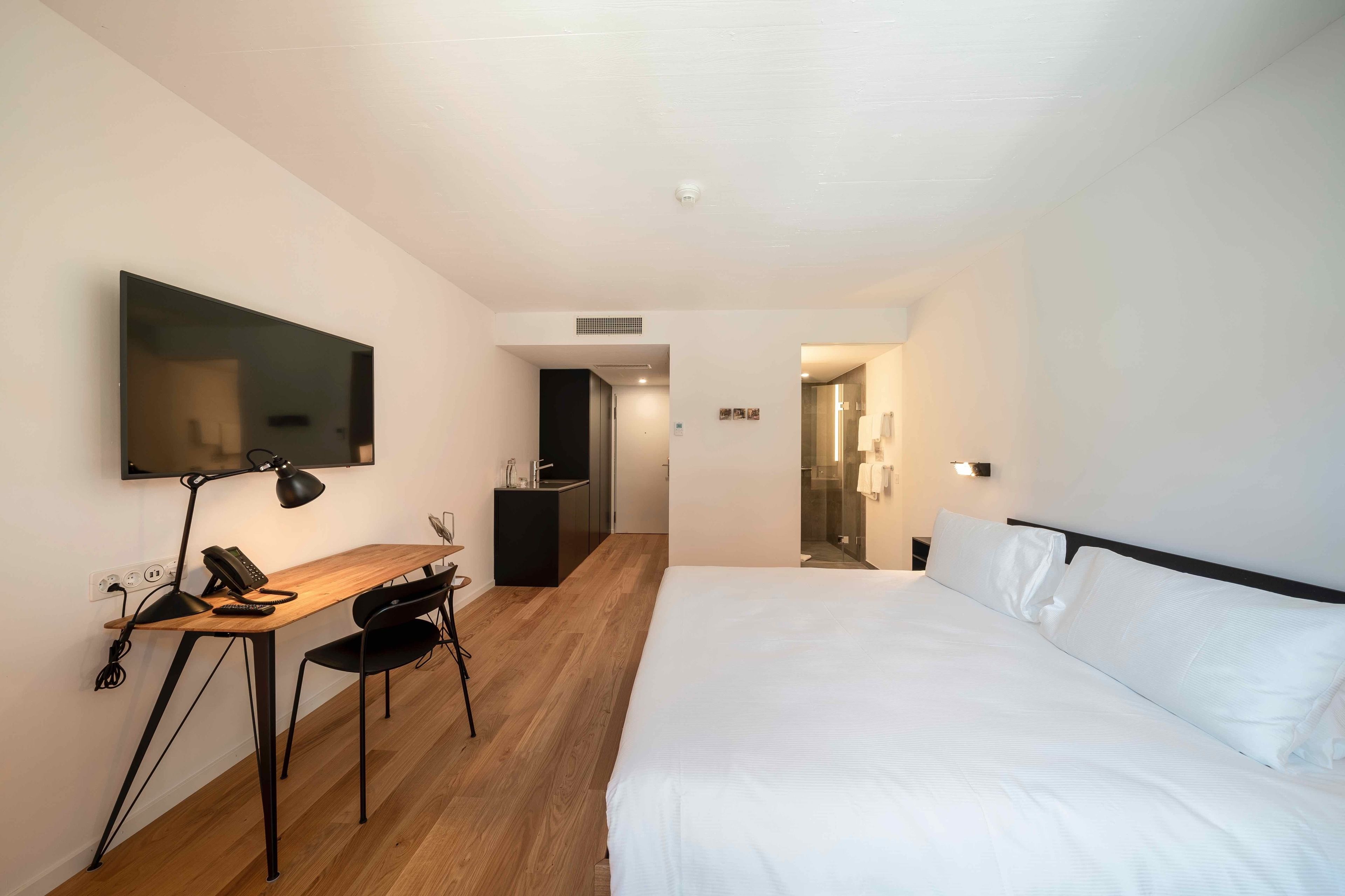 Habitación de hotel con una cama grande, un escritorio con una silla, un televisor de pantalla plana y un baño visible a través de una puerta abierta.