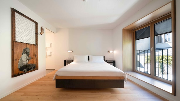 A modern bedroom with a large bed, wooden flooring, a large window, and artwork on the wall. - SET Hotel.Residence by Teufelhof Basel (Basel)