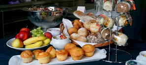 Una mesa de buffet con diversos alimentos, como frutas, bollería y pan.