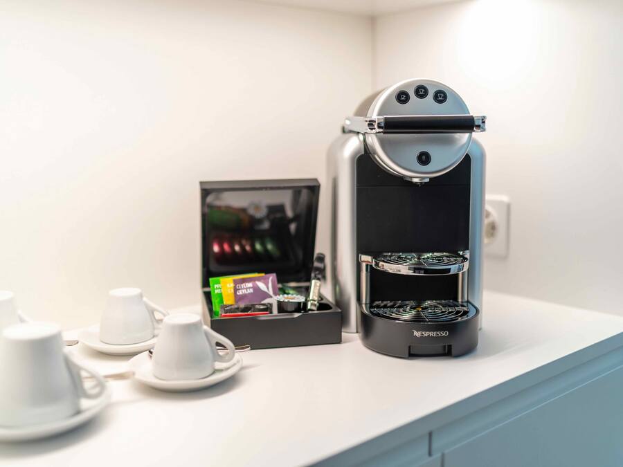 Una macchina per caffè Nespresso su un piano di lavoro bianco, con un portapodis e tazze.