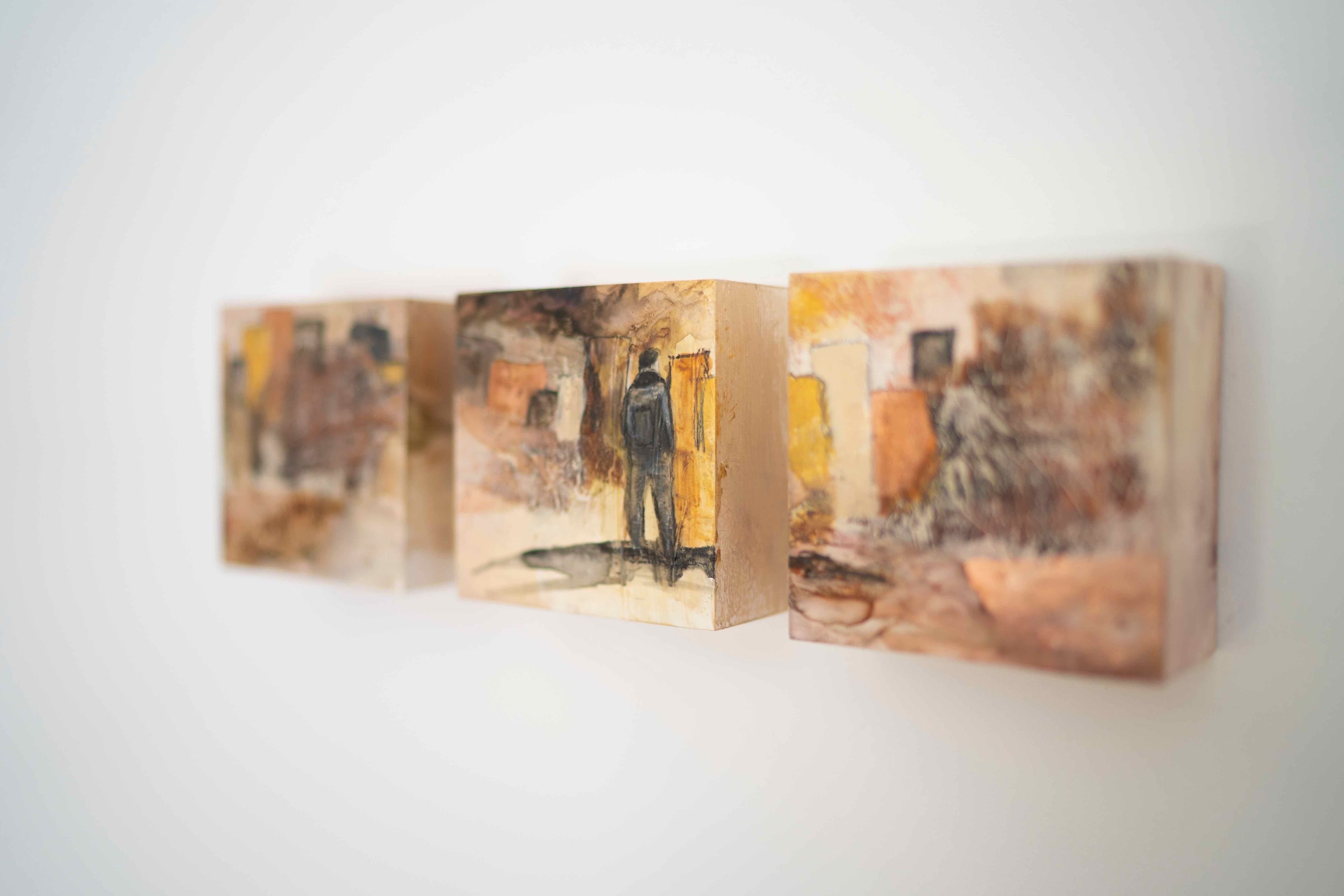 A series of three square paintings on a wall.