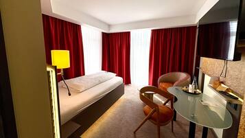 Une chambre d’hôtel avec un lit, un bureau et une chaise, une télévision et des rideaux rouges.