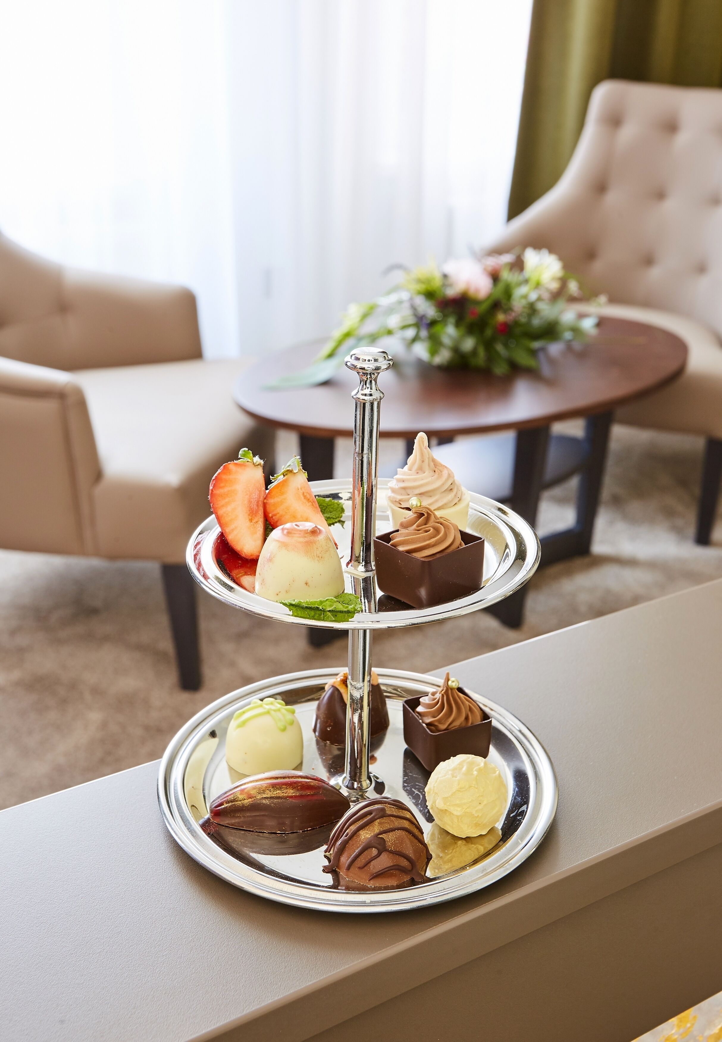 Ein mehrstufiges Desserttablett mit verschiedenen Gebäcken und Eis auf einem Tisch in einem Hotelzimmer.