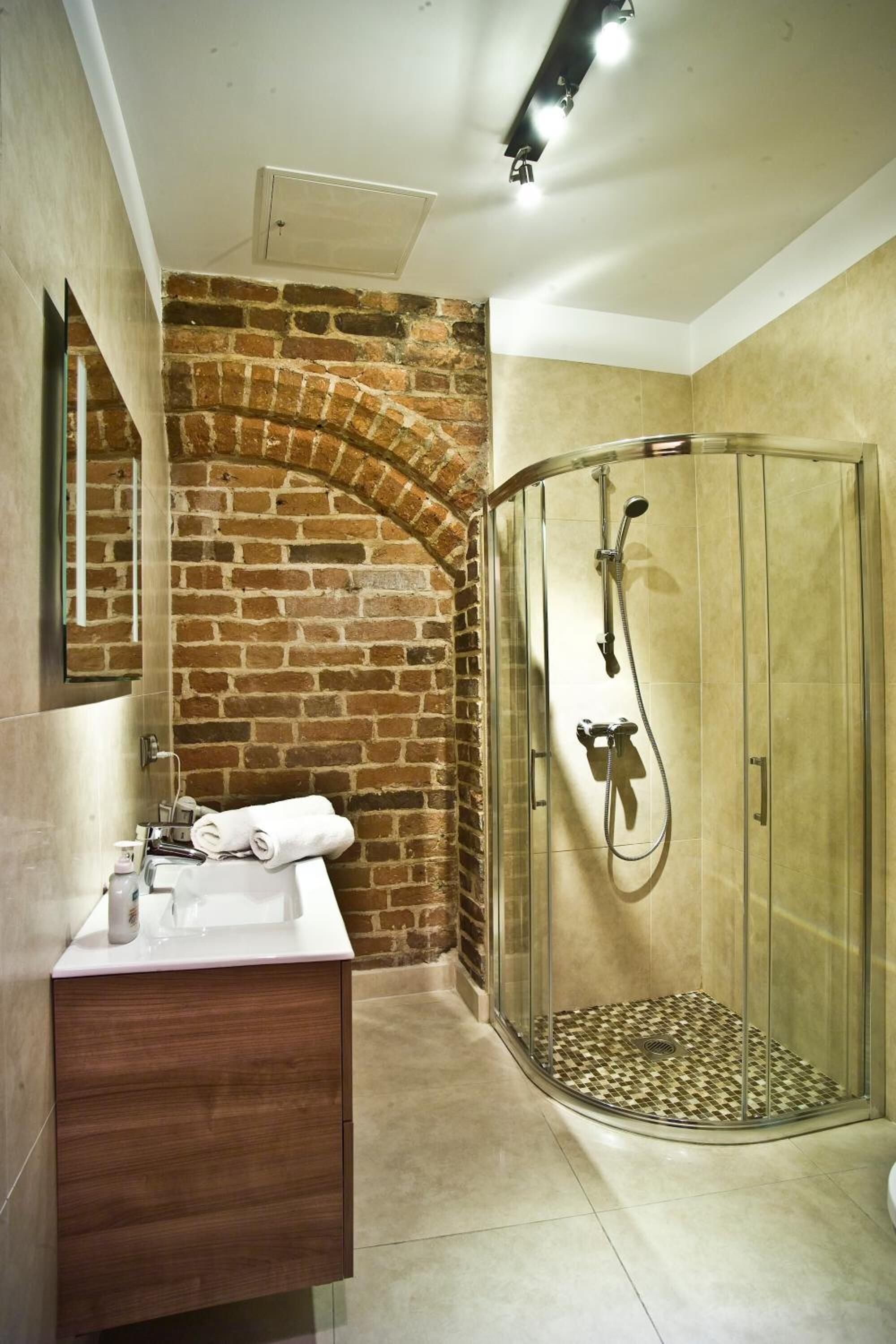 A bathroom with a glass shower enclosure, a wooden vanity, and a brick wall.