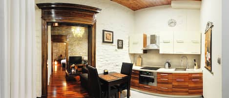 A modern kitchen with white cabinets, a stove, and a sink. There is a dining area with a table and chairs. The floor is wooden, and the ceiling is wooden with a curved design.