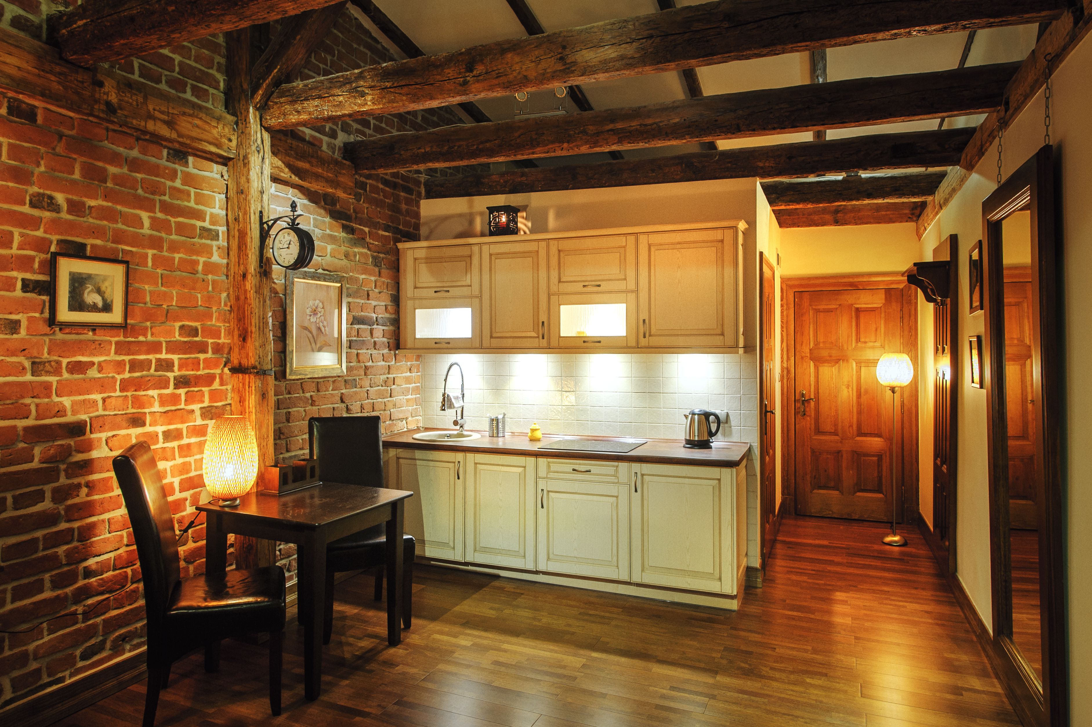 A kitchen with wooden beams, a brick wall, and a dining area with a table and chairs.