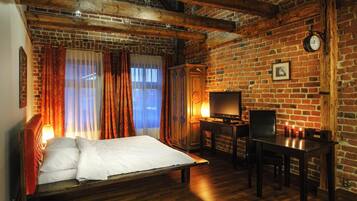 A room with a brick wall, wooden beams, a bed, a desk, and a television.