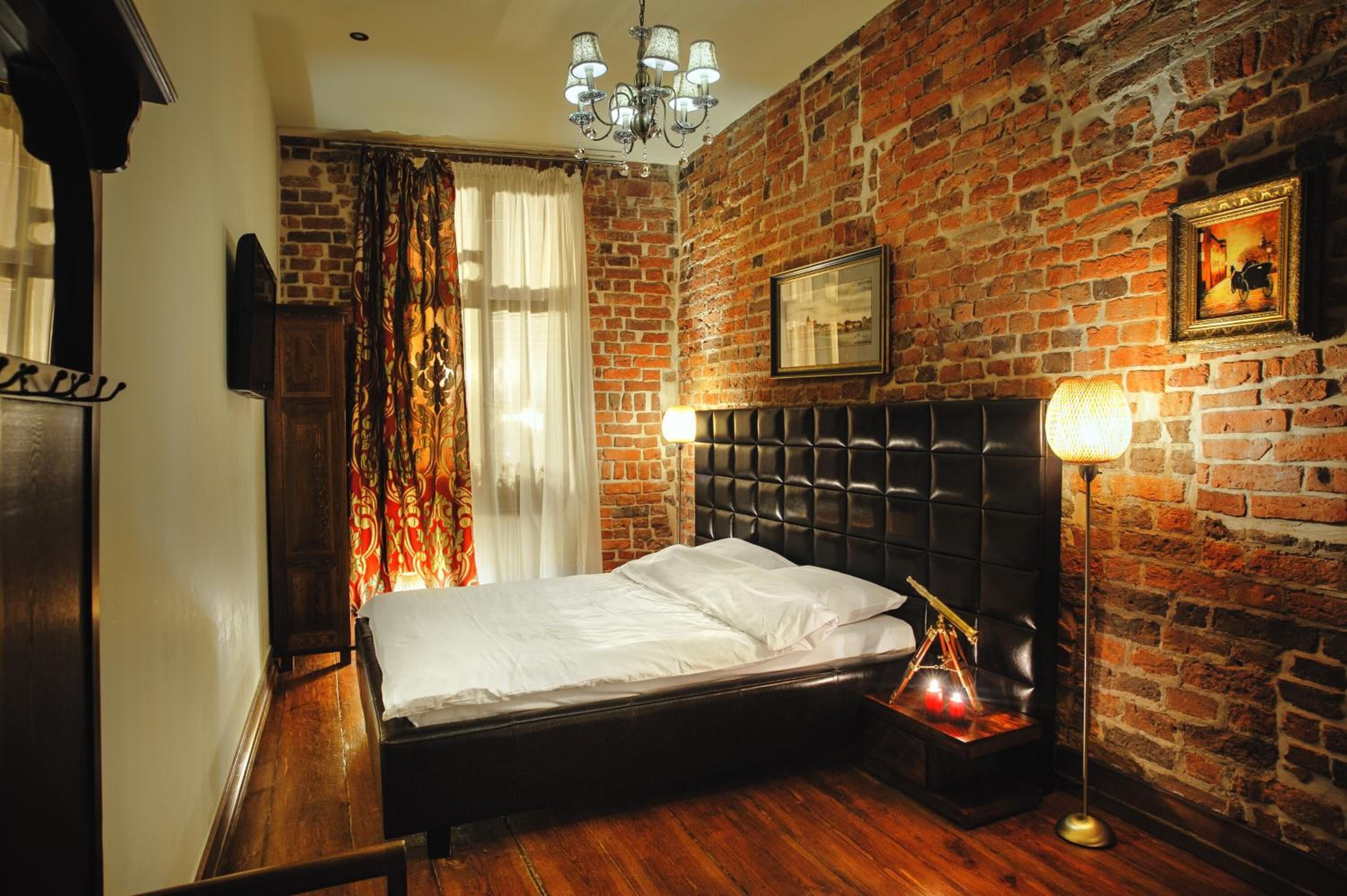 A bedroom with a brick wall, a bed with a black headboard, a chandelier, and a framed picture on the wall.