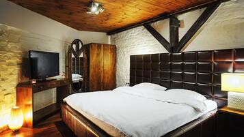 Une chambre avec un plafond en bois, un mur en pierre, une télévision, une armoire, un lit avec une literie blanche et une lampe de chevet.