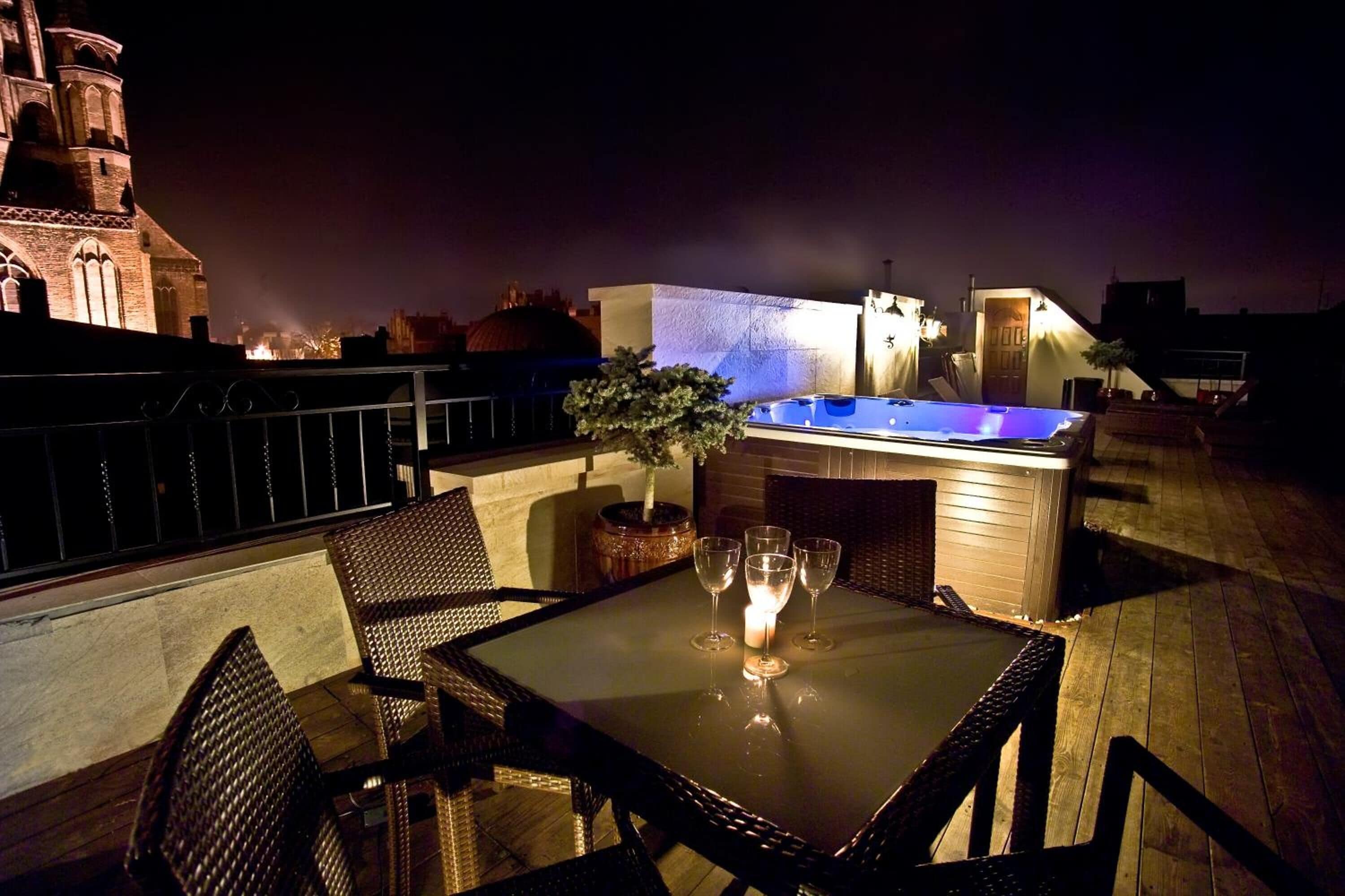 Terraza en la azotea con jacuzzi, mobiliario de mimbre y una mesa con vasos y una vela.