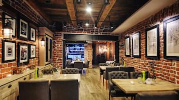 A restaurant with brick walls, wooden beams, and framed artwork on the walls. Tables and chairs are arranged for dining.